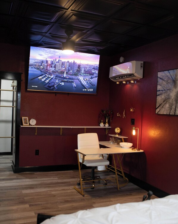 A modern room with a large TV displaying a cityscape, a desk with a chair, and a bed. - Farmhouse outskirts of Norman’s “Okla. University” fastWiFi, 2-75”TVs, KING BED (Noble)