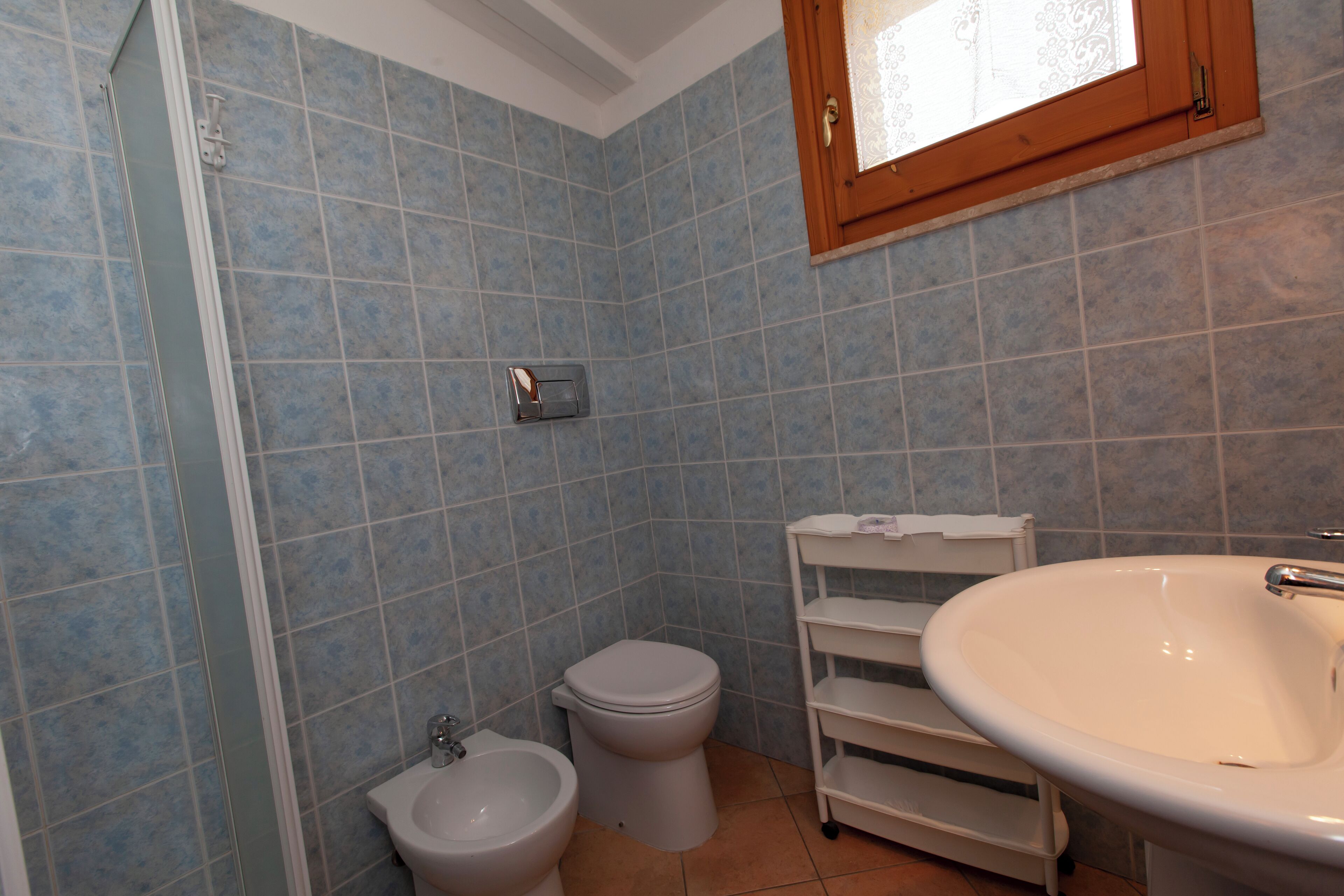 Un baño con azulejos azules, un lavabo blanco, un bidé y un inodoro.