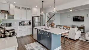 Una cocina moderna con gabinetes blancos, una isla central, electrodomésticos de acero inoxidable y lámparas colgantes.