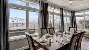 Comedor con una mesa grande dispuesta para seis personas, ventanas amplias con cortinas y un ventilador de techo.