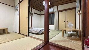 Une pièce de style japonais traditionnel, avec un sol recouvert de tatamis, un futon servant de lit, une petite table, un éventail et un extincteur.