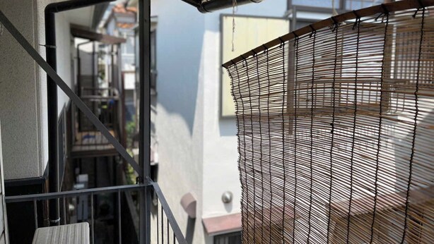 Un étroit couloir extérieur doté d’une rambarde métallique, d’un grillage et d’un escalier menant à un niveau supérieur.