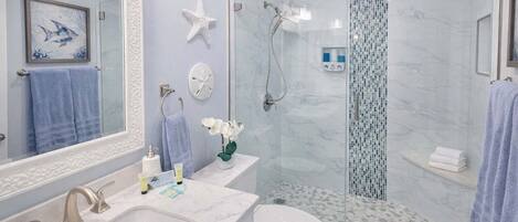 A bathroom with a marble sink, a toilet, a glass shower enclosure, and a mirror with a framed artwork.