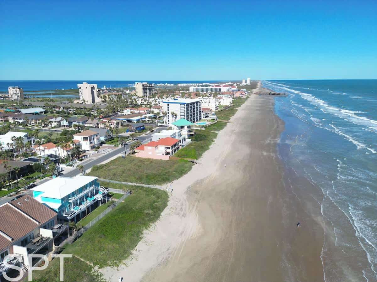 An aerial view of a coastal area with a beach, buildings, and a clear sky.