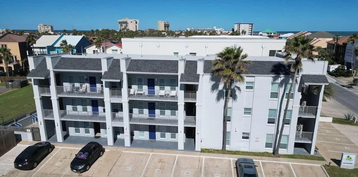 Un edificio de varios pisos con balcones, estacionamiento y palmeras.
