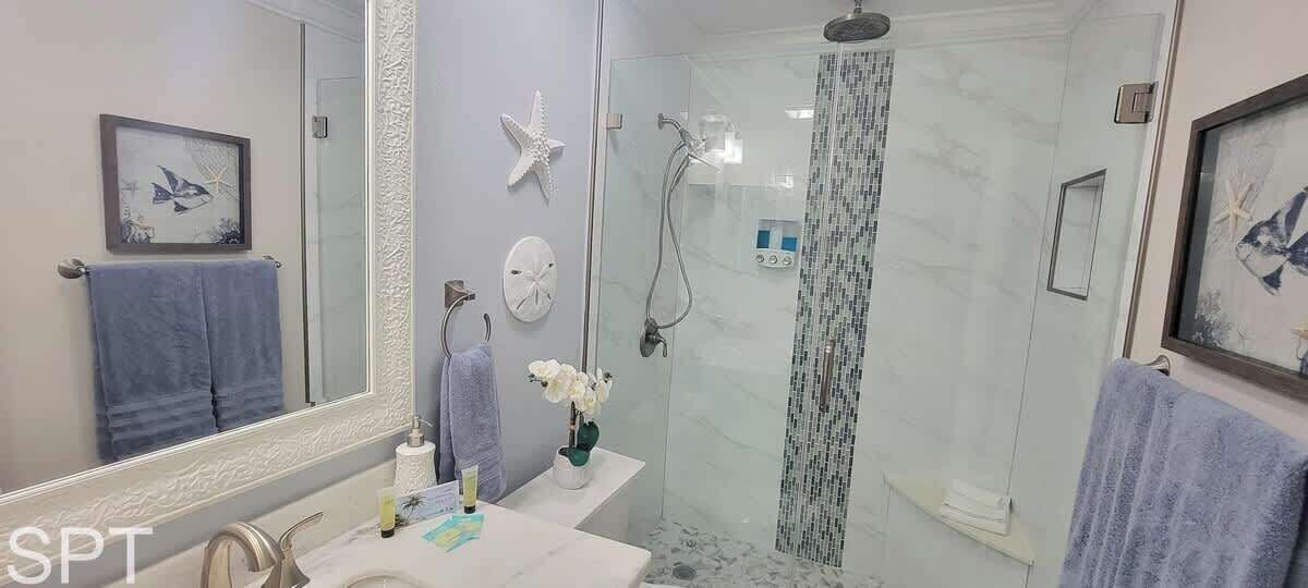 A modern bathroom with a glass-enclosed shower, a large mirror, and decorative elements like starfish and framed artwork.
