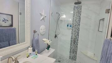 A modern bathroom with a glass-enclosed shower, a large mirror, and decorative elements like starfish and framed artwork.
