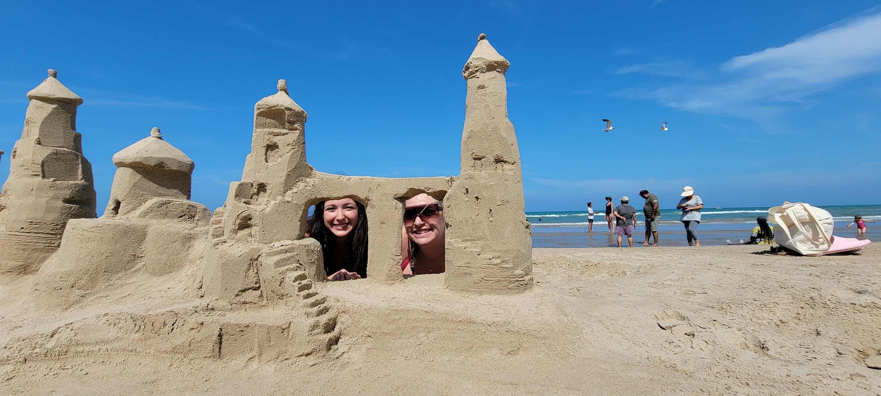 A sandy beach with a large sandcastle structure featuring multiple towers and a central entrance.