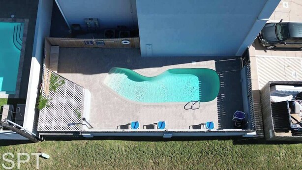 Vista aérea de una zona de piscina con piscina curva, sillas de descanso y un área de estar cubierta.