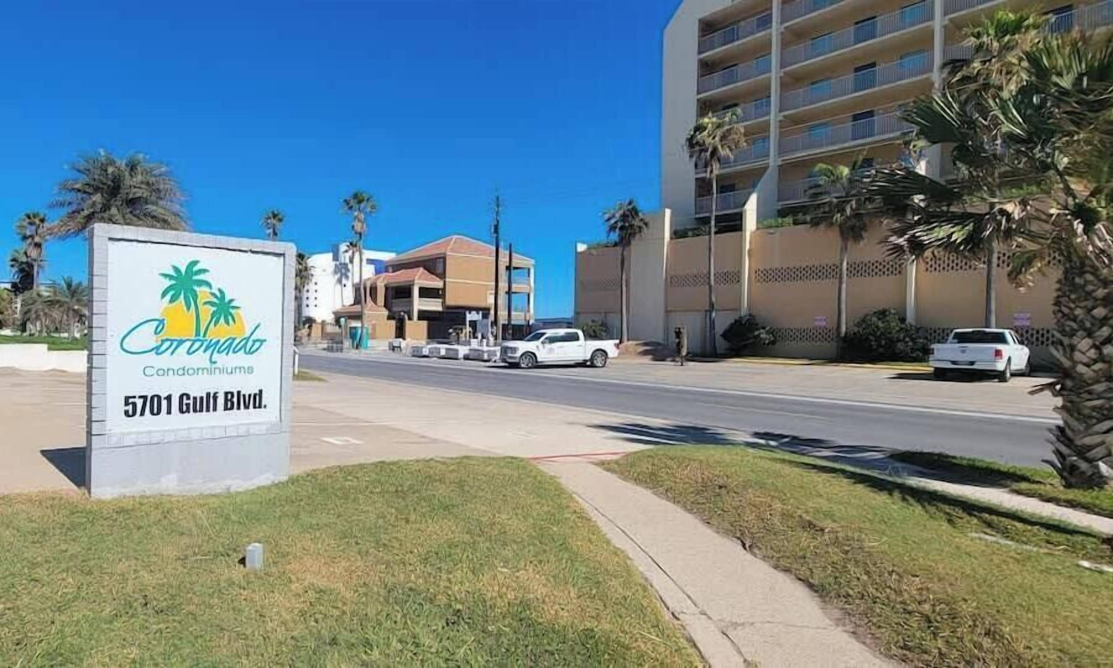 Naamplaatje voor Coronado Condominium aan 5701 Gulf Blvd, met een heldere weg en palmbomen.