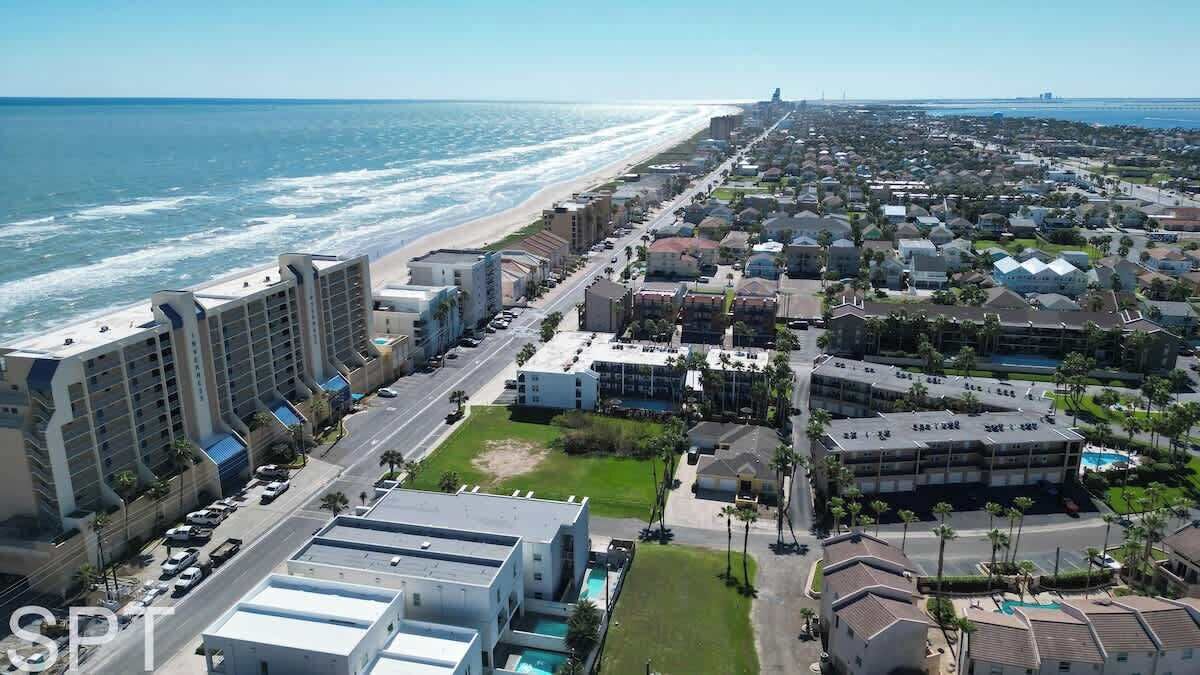 An aerial view of a coastal town with a beachfront hotel, residential buildings, and a clear view of the ocean.