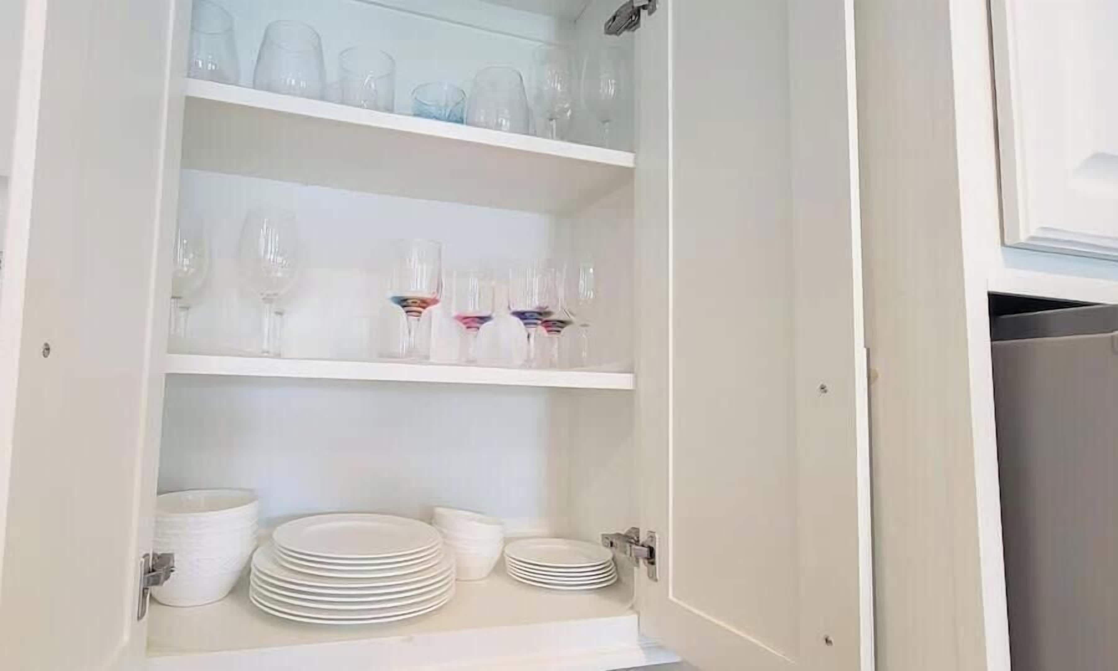 Un mueble con varios estantes que contiene copas de vino, platos y cuencos.