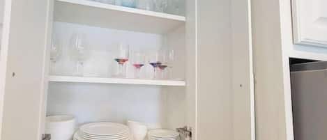 Un mueble con varios estantes que contiene copas de vino, platos y cuencos.