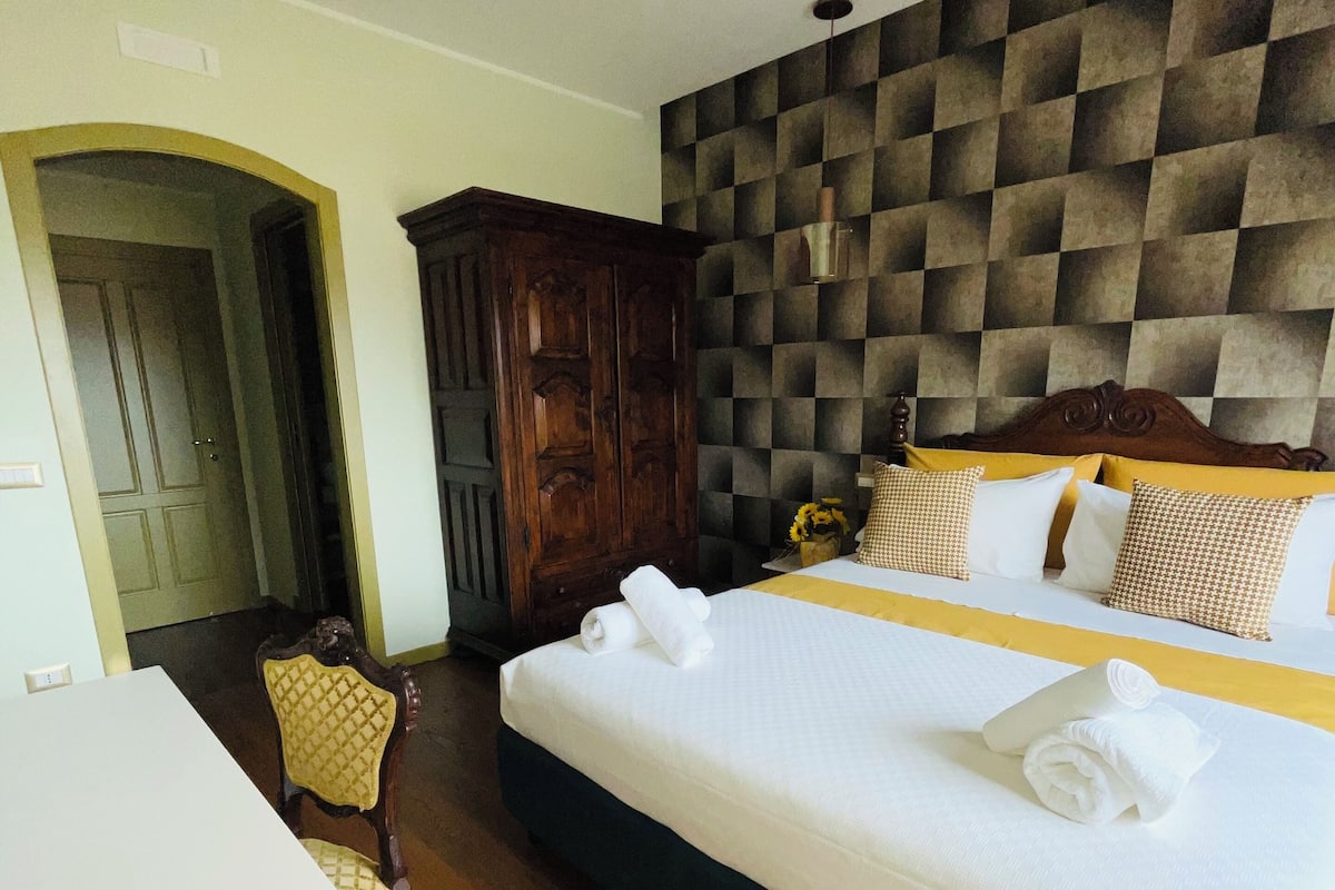 A hotel room with a large bed, a wooden wardrobe, a desk, and a chair.