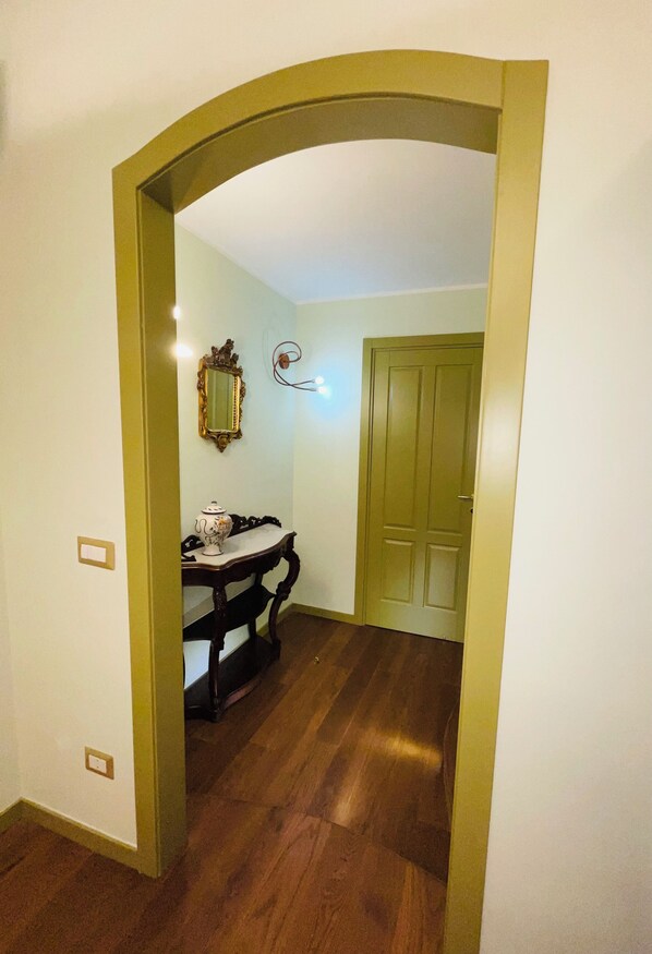 Un corridoio con pavimento in legno, un tavolo da pranzo con tovaglia bianca e azzurra e una porta verde in fondo.