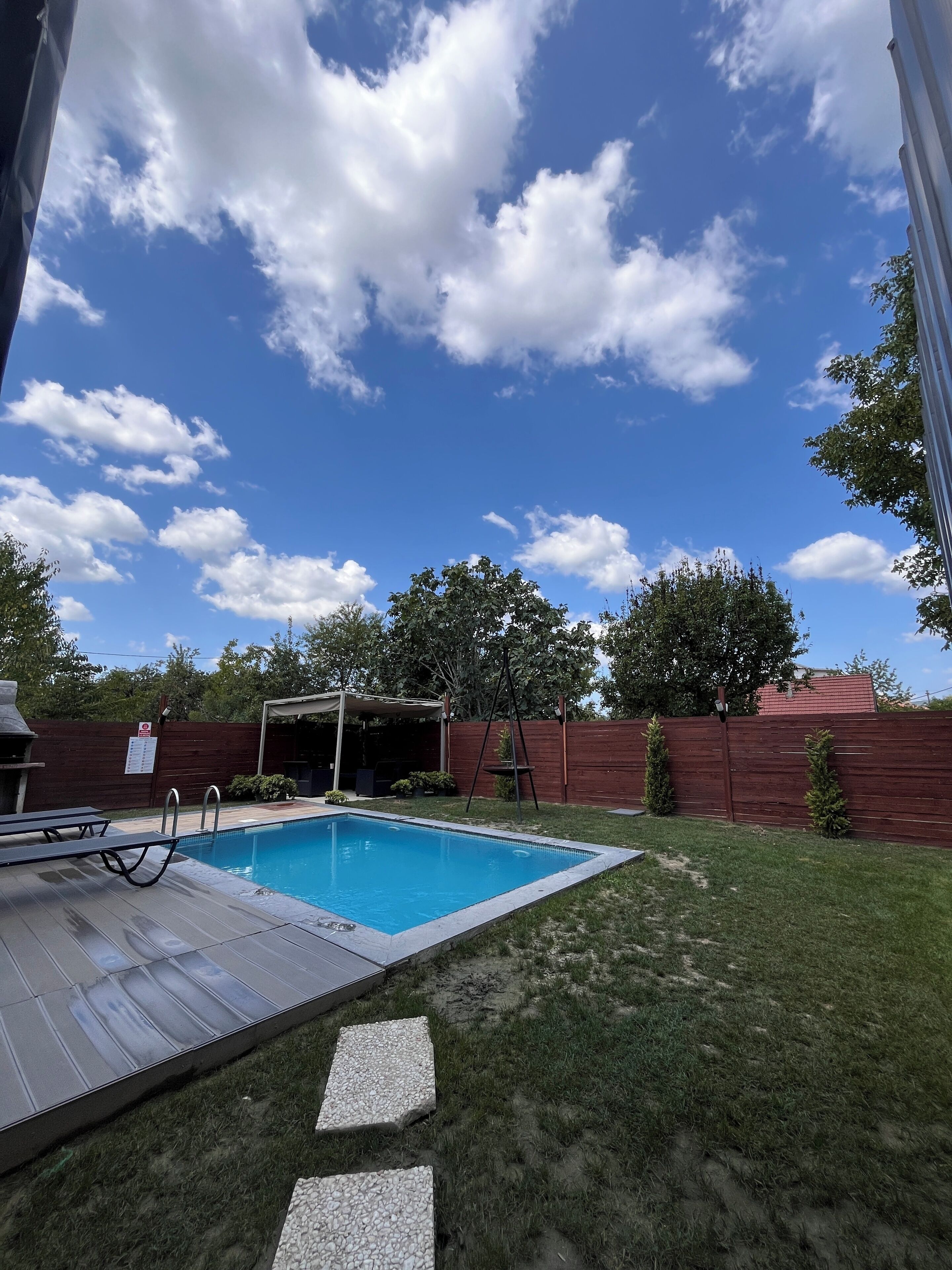 Un jardin avec une piscine, un patio couvert et une clôture en bois.