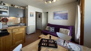 A compact kitchen with a dining area, a purple sofa, and a painting on the wall. - (7.B17) Appartement skis aux pieds Les Menuires (Les Menuires)