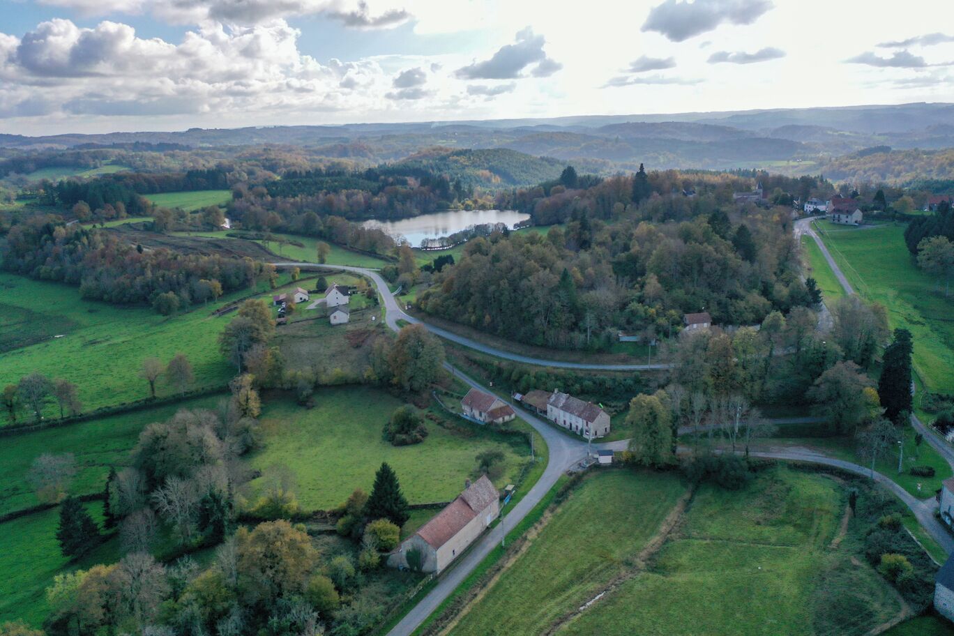 Une vue aérienne d’une zone rurale, avec une route sinueuse, des champs verdoyants et des bâtiments dispersés.