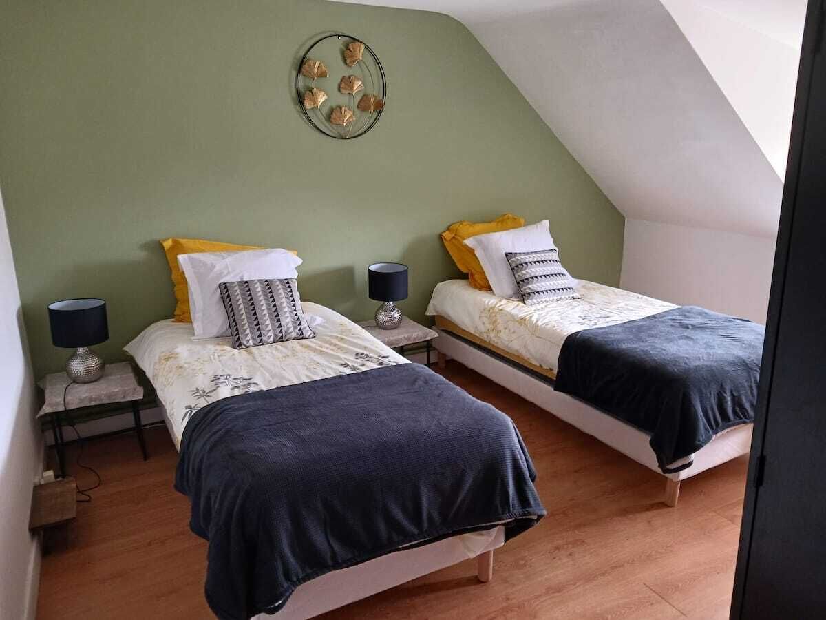 Una habitación con dos camas, cada una con mesita de noche y lámpara, un adorno en la pared y un techo inclinado.