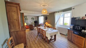 A dining area with a wooden table set for four, a hanging light fixture, and a view of the outdoors through a window. - Country cottage La Belle du Clocher - All inclusive (Saint-Pardoux-d'Arnet)