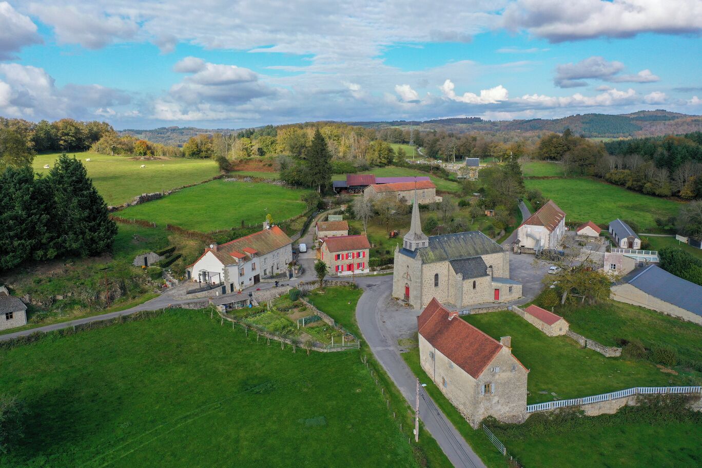 A rural village with stone buildings, a church, and green fields.