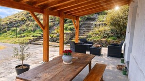 An outdoor wooden pergola with a table and chairs, surrounded by potted plants and a stone staircase in the background. - Country cottage La Belle du Clocher - All inclusive (Saint-Pardoux-d'Arnet)