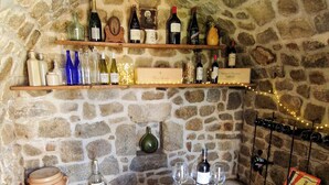 A stone-walled cellar with wine bottles on shelves and a barrel with grapes. - Country cottage La Belle du Clocher - All inclusive (Saint-Pardoux-d'Arnet)