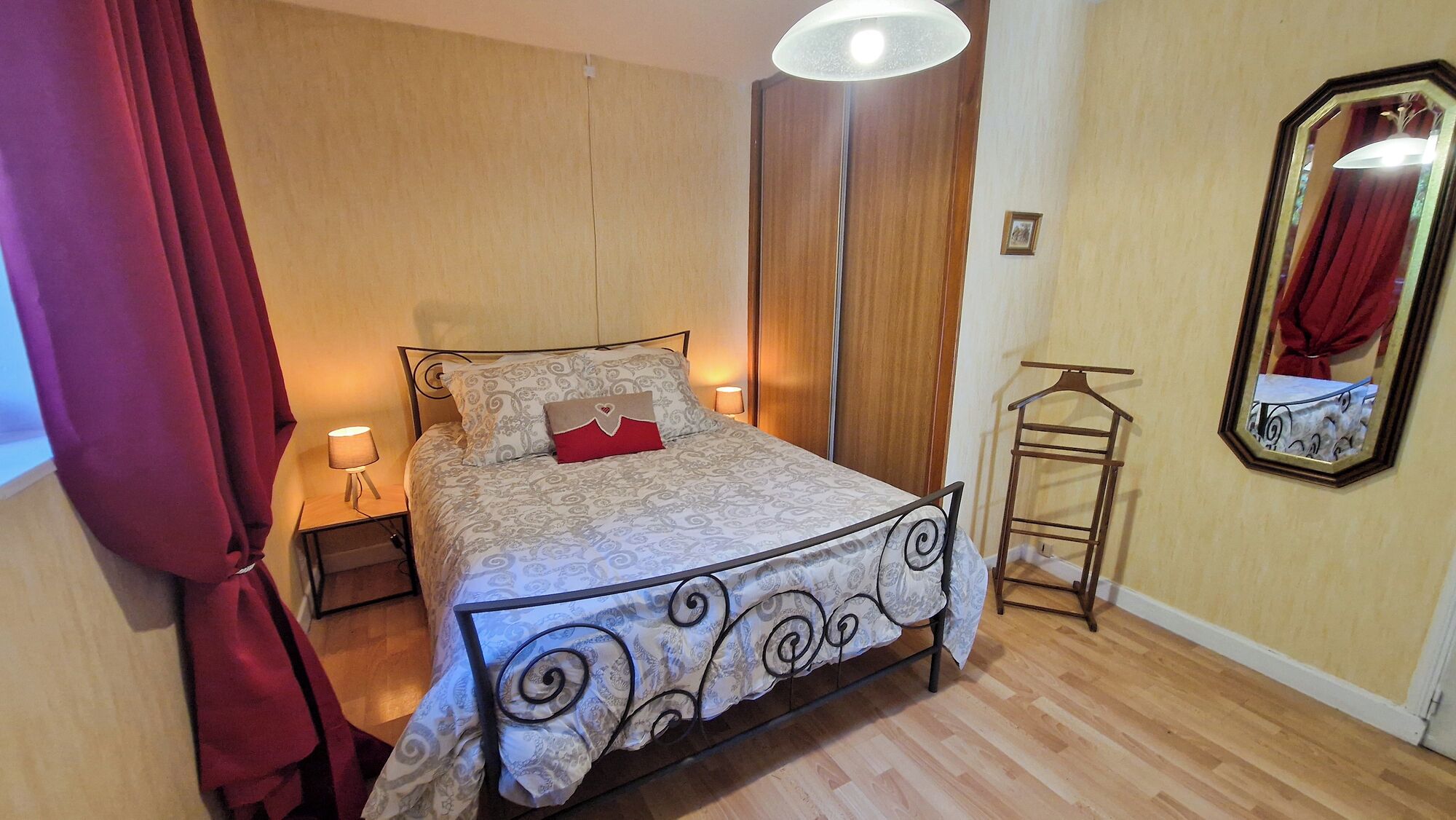 Un dormitorio con cama, mesita de noche, lámpara colgante, armario, espejo y perchero.