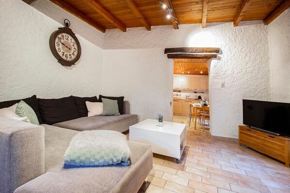 A cozy living room with a sofa, a coffee table, a TV, and a kitchen in the background.