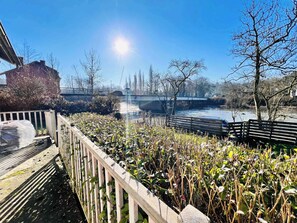 A riverside walkway with a wooden fence, a bench, and a bridge in the background. - Riverside Cabin Surrounded by Nature for Two (Esneux)