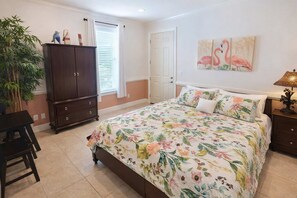 A bedroom with a bed, a nightstand, a dresser, a window with curtains, a door, and a painting of flamingos. - Island Time #4 (South Padre Island)
