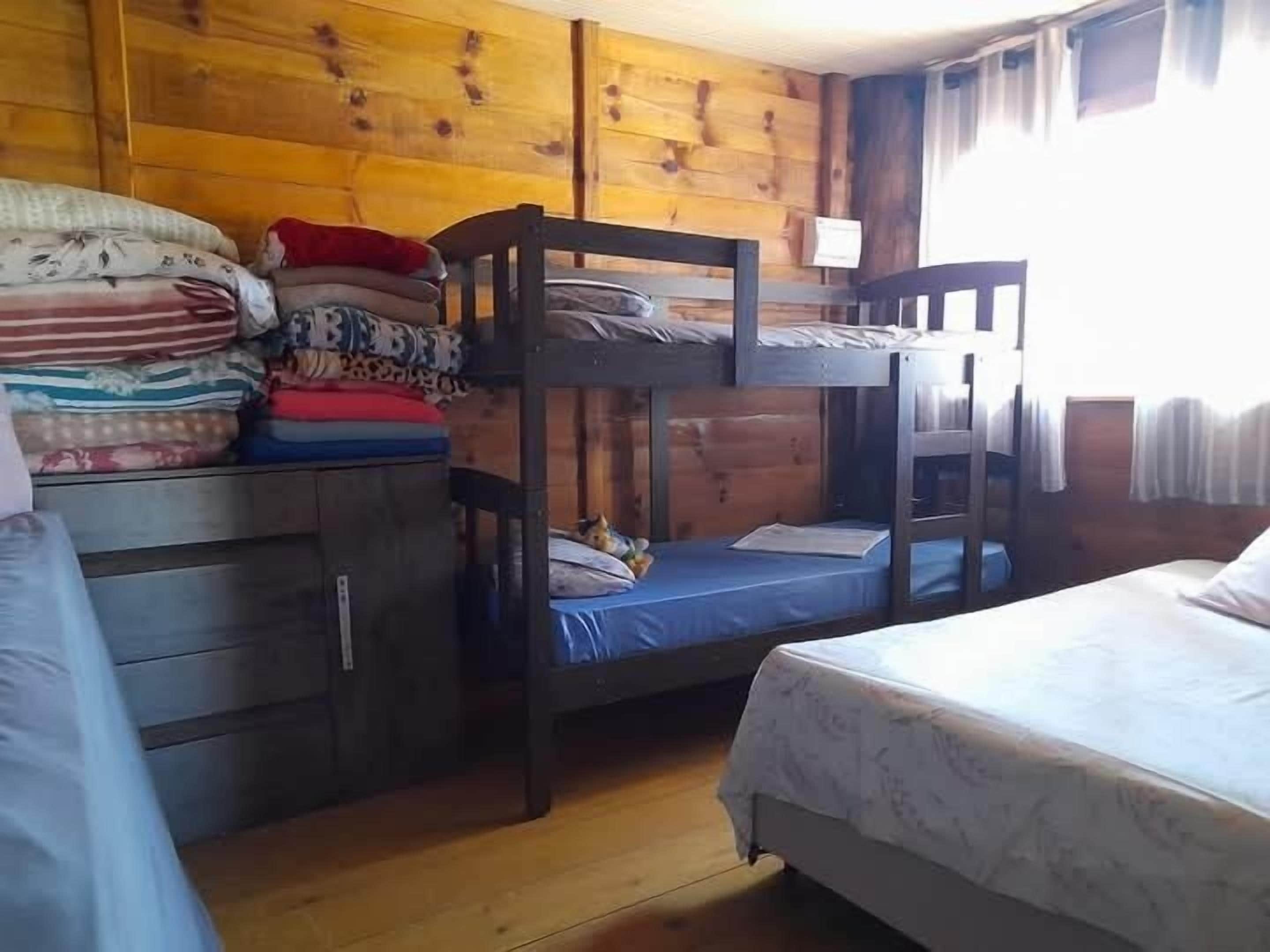 Een slaapkamer met stapelbed, houten wanden, een bureau met lades en een bed met een witte hoes.