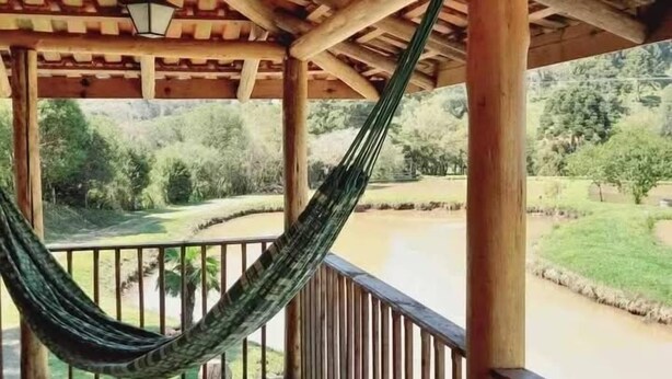Una terraza de madera con una hamaca, barandilla de madera y vistas a un río y vegetación.