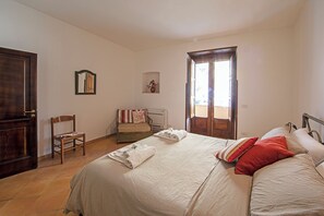 Ein Schlafzimmer mit Bett, Stuhl, kleinem Tisch, Spiegel und Tür.