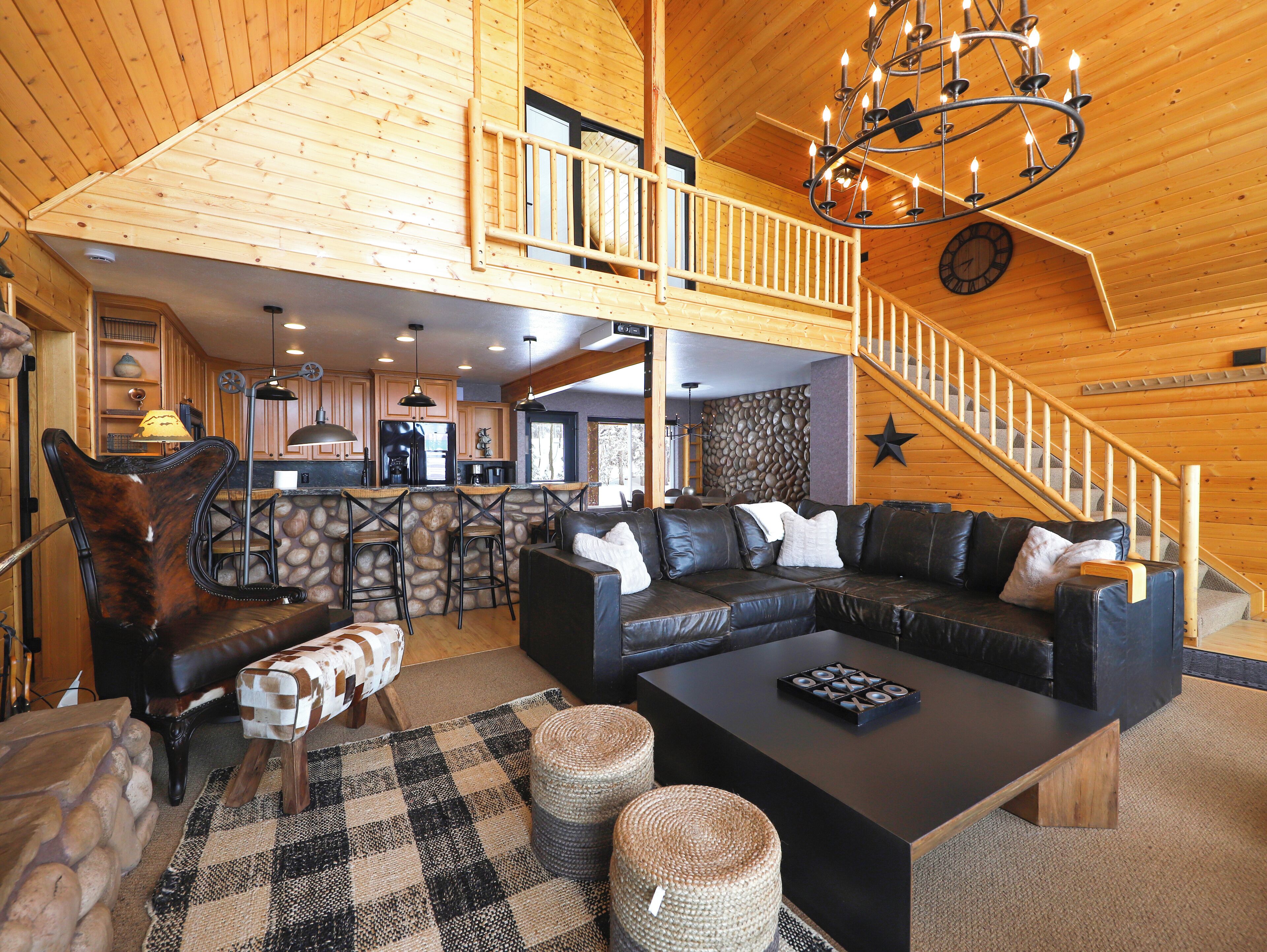 A spacious living area with a large black sectional sofa, a wooden ceiling, and a stone accent wall.
