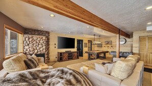 Un salón acogedor con chimenea, un televisor de pantalla plana grande, mesa de billar y un sofá cómodo.