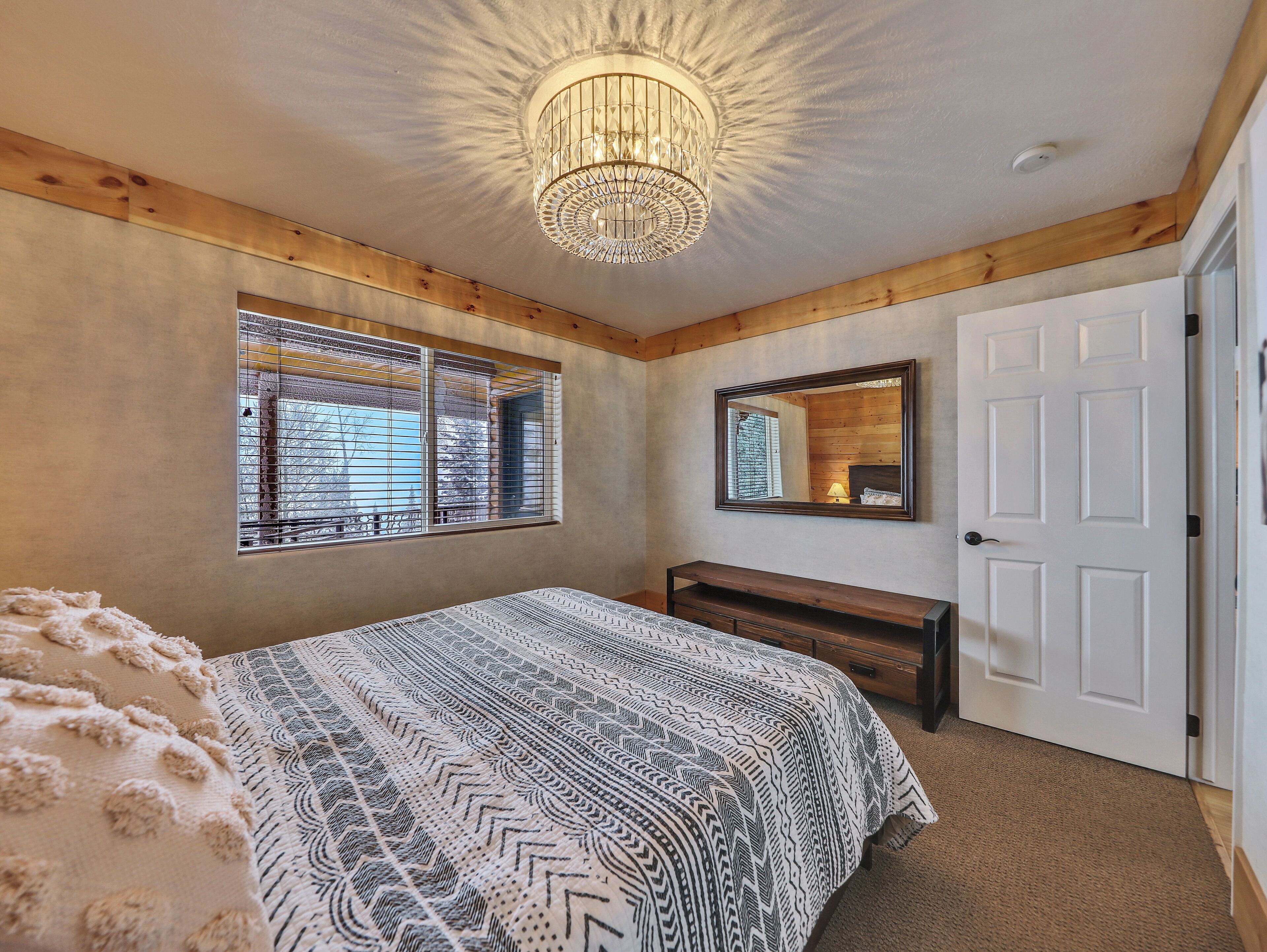 A bedroom with a bed, a bench, a large mirror, and a window with blinds.