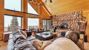Interior acogedor de una cabaña de troncos con chimenea de piedra, sofás de cuero y amplias ventanas con vistas a árboles nevados.