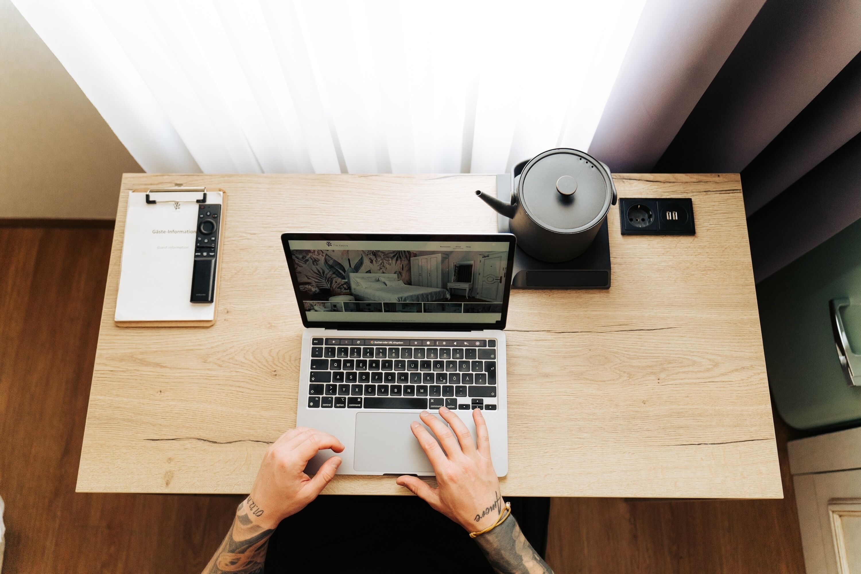 Un ordinateur portable sur un bureau en bois, avec une bouilloire et une multiprise.