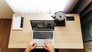 Un ordinateur portable sur un bureau en bois, avec une bouilloire et une multiprise.
