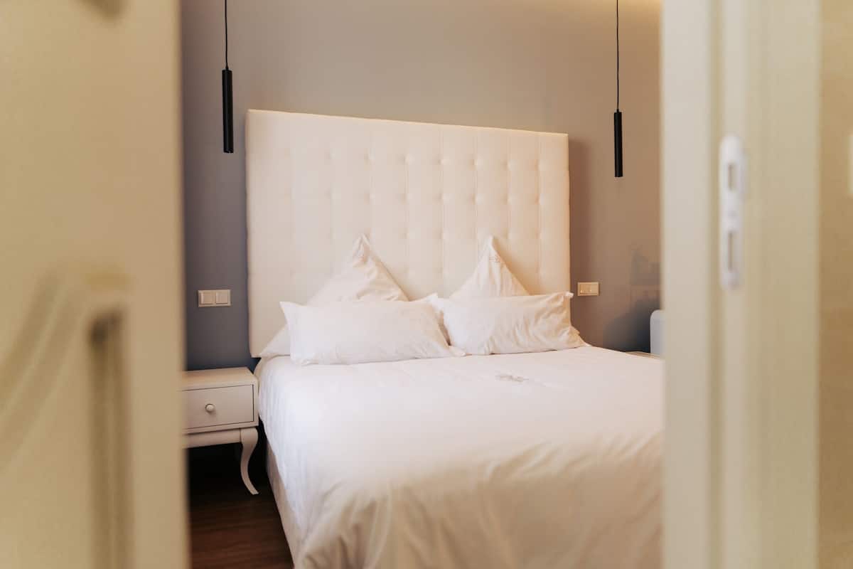 A neatly made bed with a tufted headboard, a bedside table, and a hanging light fixture.