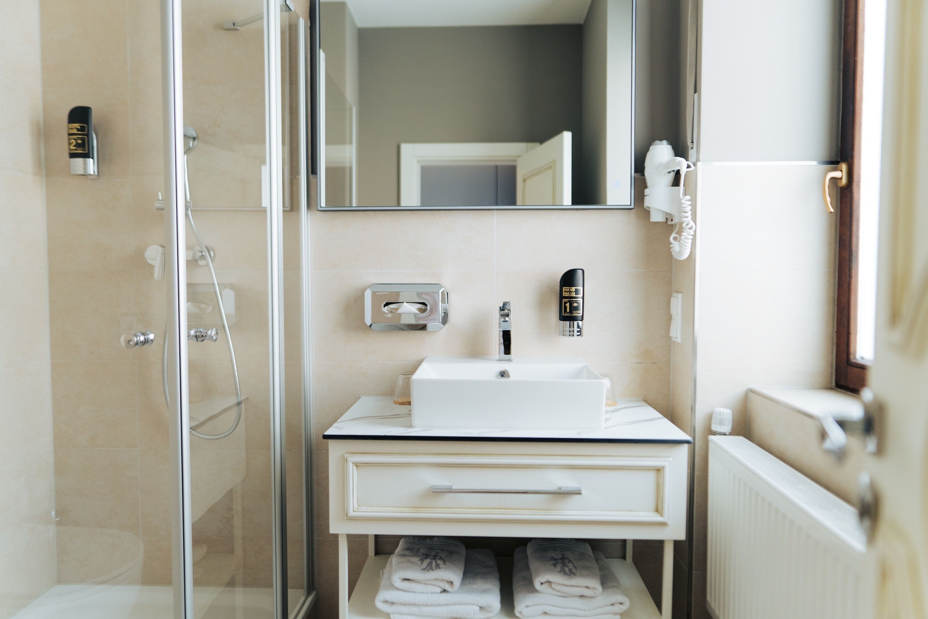 A modern bathroom with a glass shower enclosure, a white sink with a mirror above, and neatly folded towels on a shelf.