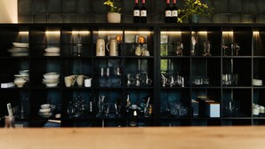 A bar area with shelves of glassware, bottles, and potted plants. - The Kepos Hotel Erlangen (Erlangen)