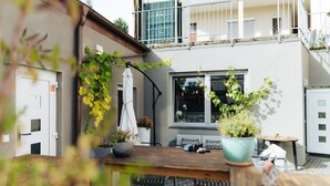 A courtyard with a wooden table, potted plants, a sofa, and a window overlooking a building. - The Kepos Hotel Erlangen (Erlangen)