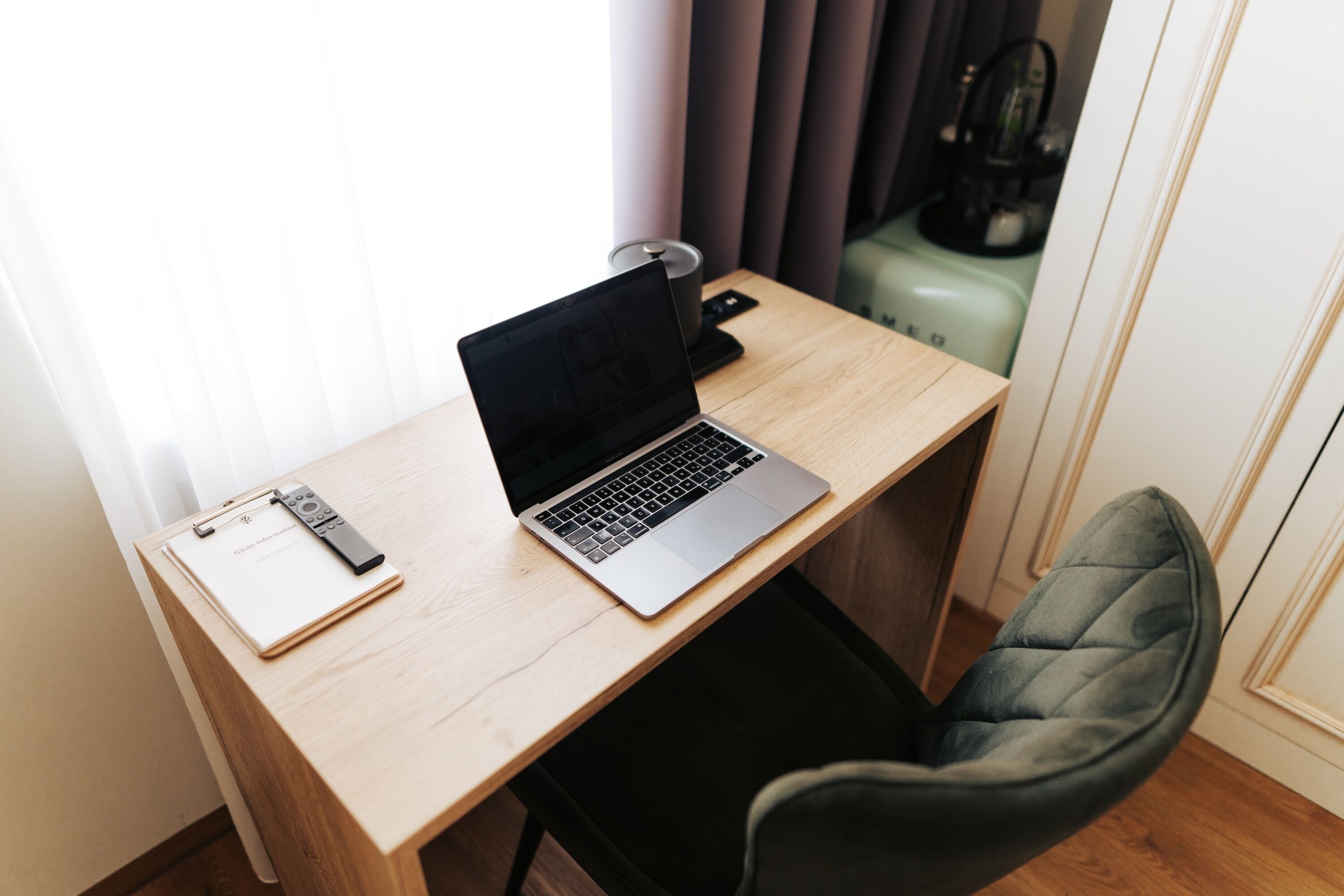 A wooden desk with a laptop, a remote control, and a clipboard.