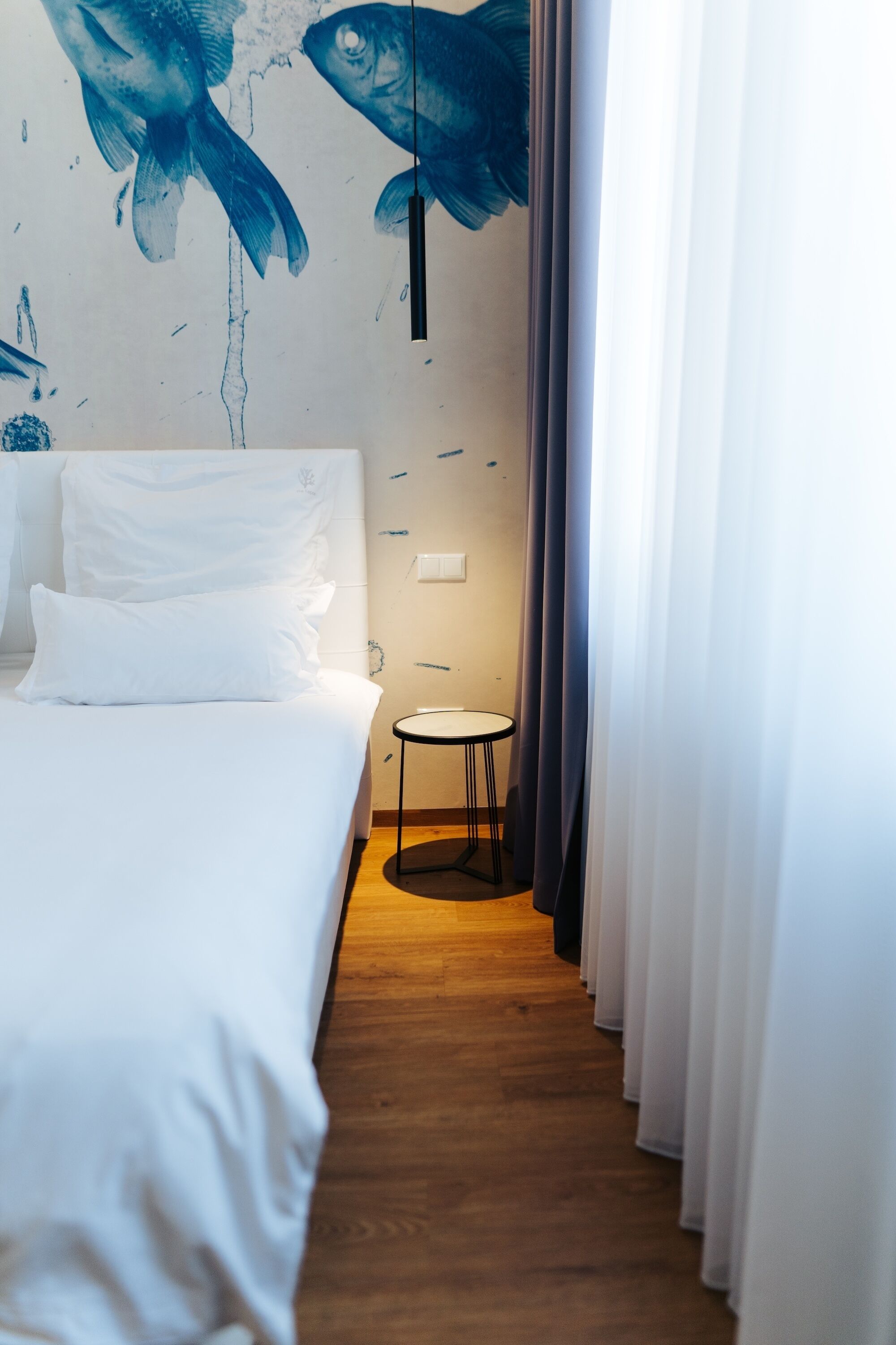 A hotel room with a bed, a small round table, and a wall mural of fish.