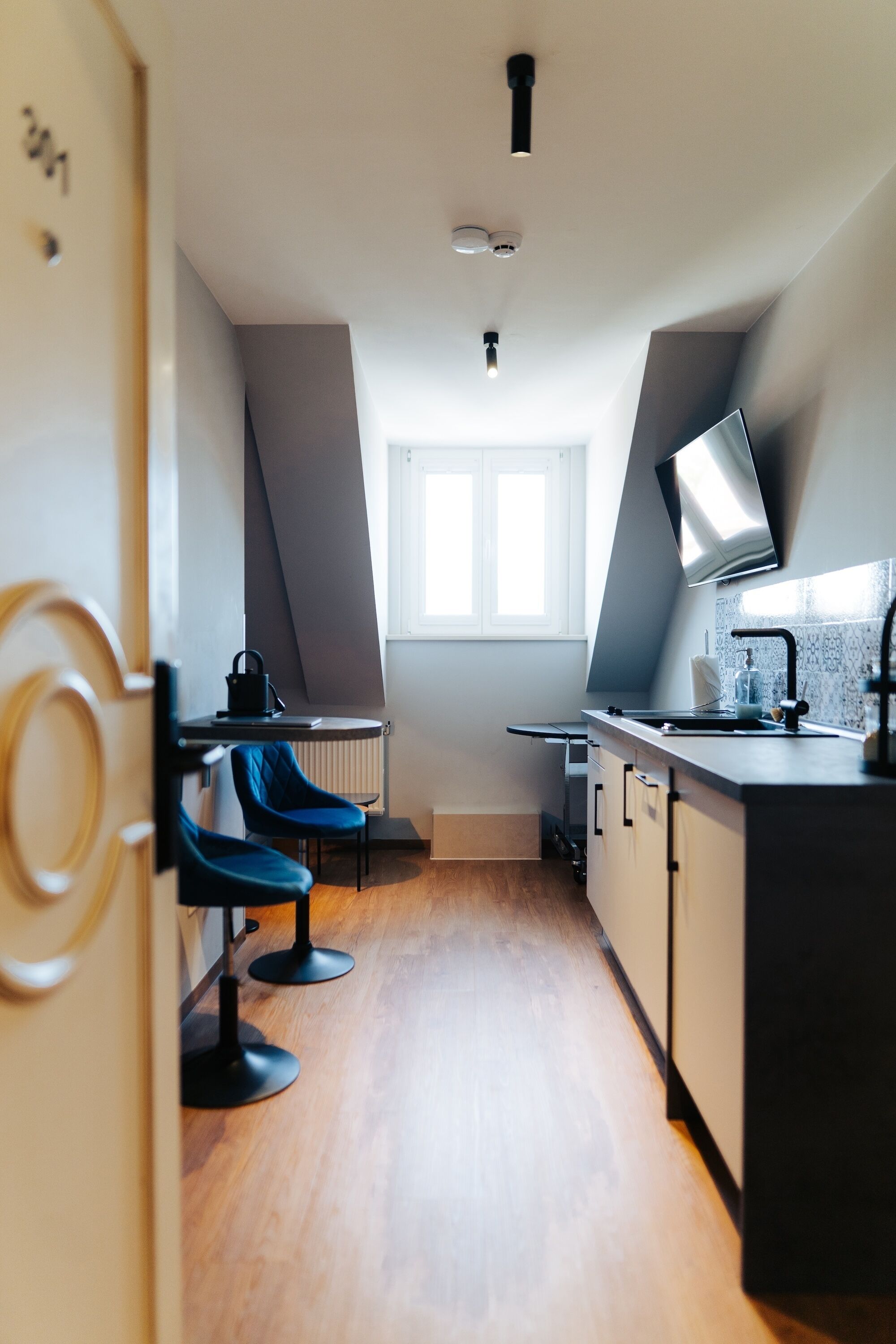 A modern kitchen with a built-in stove, a sink, and a window. There are two blue chairs and a small table.