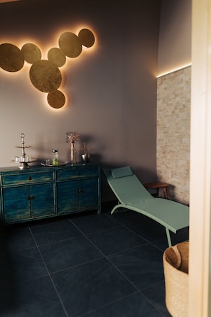 A spa room with a massage table, a blue cabinet with decorative items, and a wall-mounted light fixture. - The Kepos Hotel Erlangen (Erlangen)