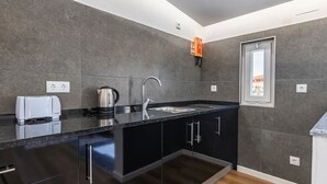 Una cocina moderna con gabinetes oscuros, un hervidor de acero inoxidable, un lavamanos integrado y una ventana con vistas.