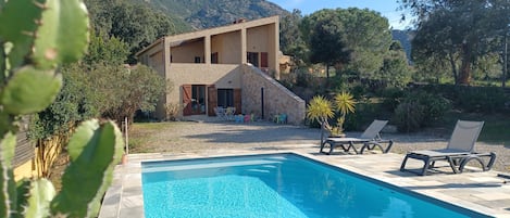 A poolside area with a pool, lounge chairs, and a stone building with a balcony.